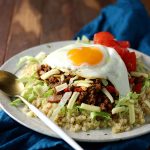 A plate full of taco rice ingredients made with cauliflower rice, taco meat, lettuce, tomato and cheese.