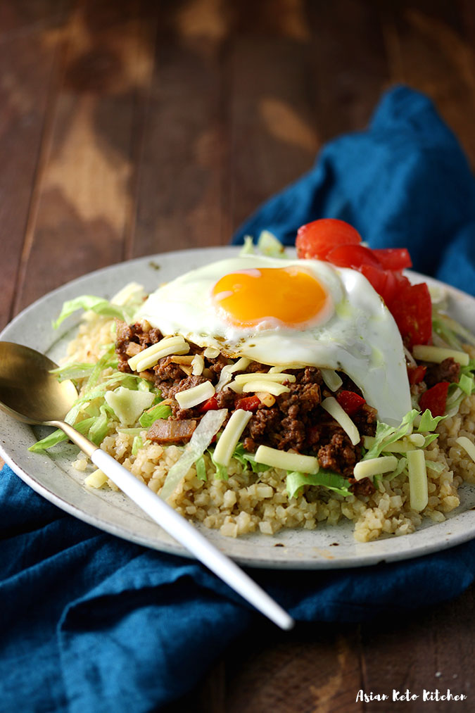 A plate full of taco rice ingredients made with cauliflower rice, taco meat, lettuce, tomato and cheese.